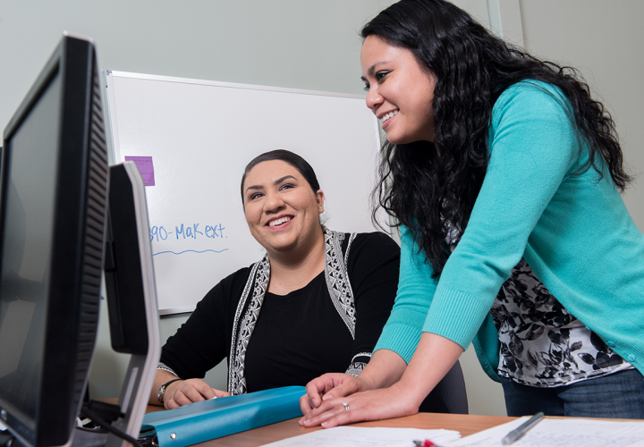 Woman in blue sweater looking at computer with another woman