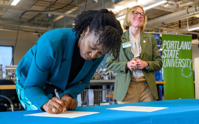 PCC President Adrien Bennings signs as PSU President Ann Cudd watches