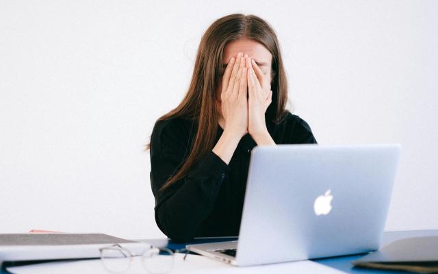 Person sitting at a laptop with head in hands, representing workplace stress and emotional strain