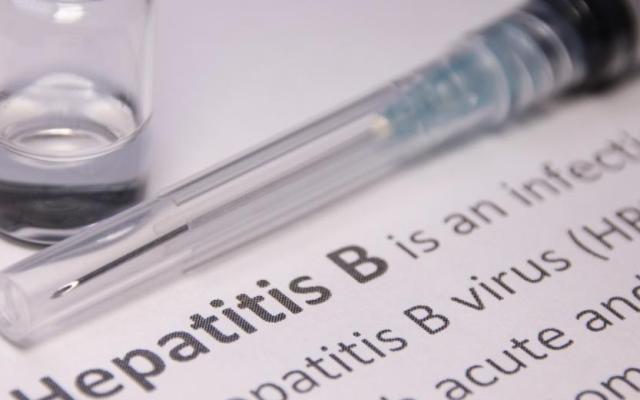Close-up of a syringe and vial next to printed information about hepatitis B