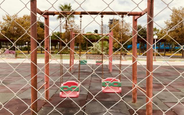 Empty playground swings seen through a rusty chain-link fence
