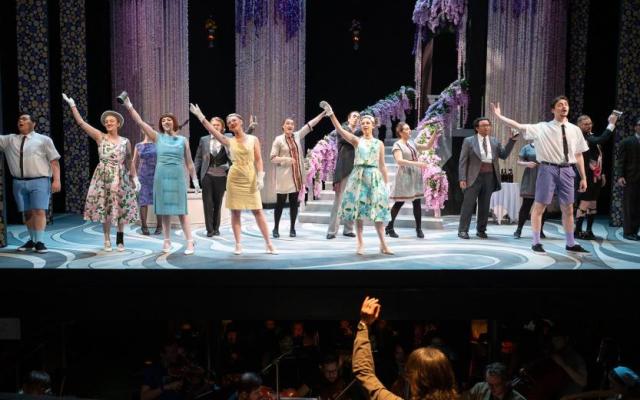 Large cast of performers in The Merry Widow don colorful costumes and sing on a theater stage at PSU with an orchestra pit in the foreground
