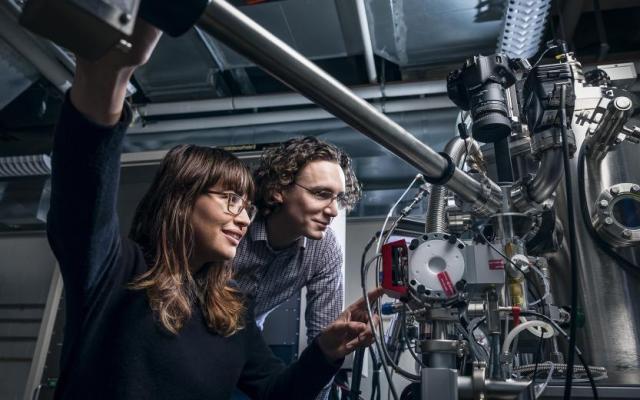 Two students in a laboratory use a large high-tech microscope for semiconductor research