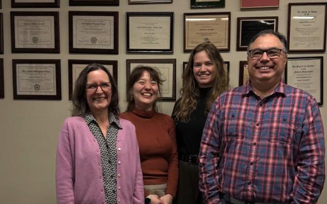 Four smiling members of the Pacific Historical Review editorial team standing in front of a wall covered in framed awards
