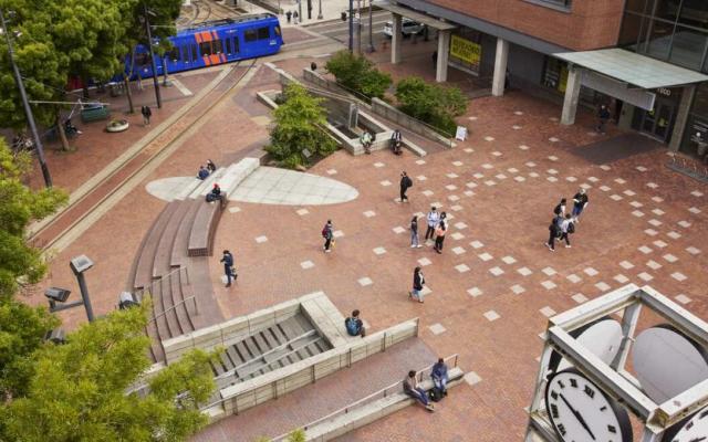Aerial view of students and pedestrians walking through the urban brick plaza at Portland State University next to a MAX light rail train