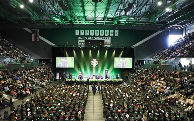 Graduates sit in the arena of the Viking Pavilion during Portland State University's commencement ceremony under green stage lighting