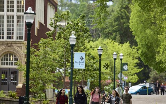 Students walk past Portland State banners on campus along a tree-lined walkway