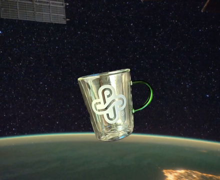 A glass mug with the Portland State University logo floats in space above Earth, with stars and a satellite panel in the background