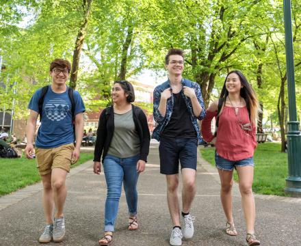 Four diverse students with backpacks walking and smiling together through the sunlit South Park Blocks on the Portland State campus