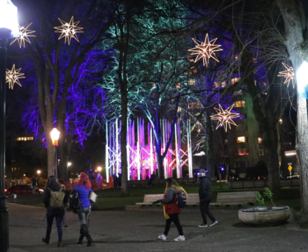 Nighttime scene at the Portland Winter Light Festival, where glowing art installations and star lights brighten a park as people walk through