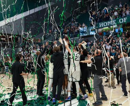Portland State basketball players celebrate on the court under falling green and white streamers