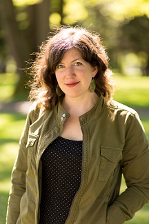 White woman with short brown hair and a green jacket against a blurred nature backdrop