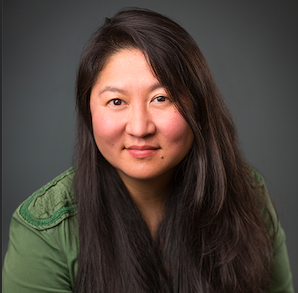 A women smiling with black hair and wearing a green jacket.