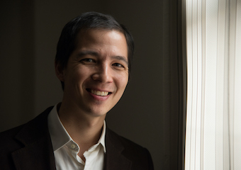 Alan Teo, a multiracial man with short, dark hair, smiling near a window.