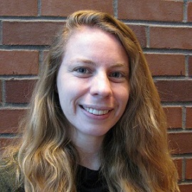 Smiling White, red-haired woman against a brick backdrop