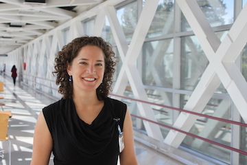 Image of Honora Englander, a younger looking woman with dark curly brown hair in professional clothes, smiling.