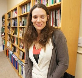 Picture of Anaïs Tuepker, a white woman with long straight brown hair and brown eyes, standing in front of bookcases and smiling.