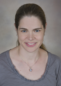 White woman with brown hair in pony tail smiling at camera.