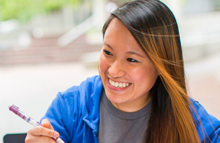 Student smiling with pen in hand and notebook open