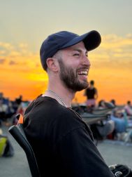 Person sitting in a chair on the lawn at sunset. They are wearing a black baseball cap and a black shirt.