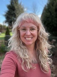 Blonde woman with pink highlights on her fringe smiling to the camera