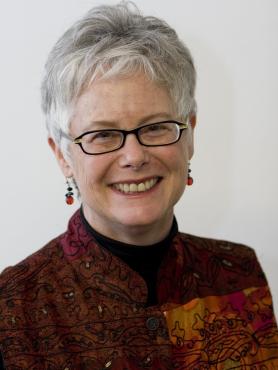 Photo of Lynn Fox wearing a burgundy jacket and glasses, smiling. 