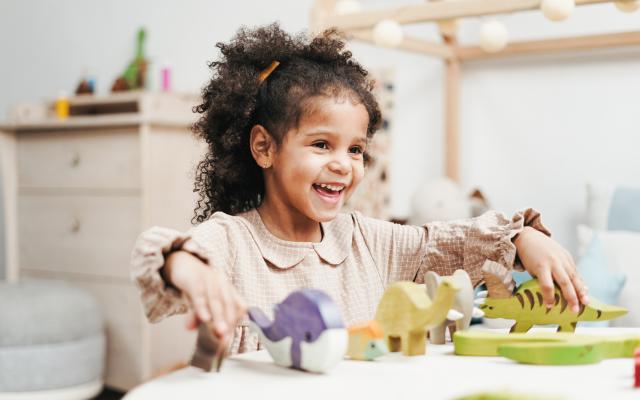 Laughing Young Girl Playing with Wooden Toys on White Table