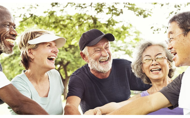 The photograph depicts a group of elderly individuals who are dressed in sportswear and participating in a team bonding hand gesture.