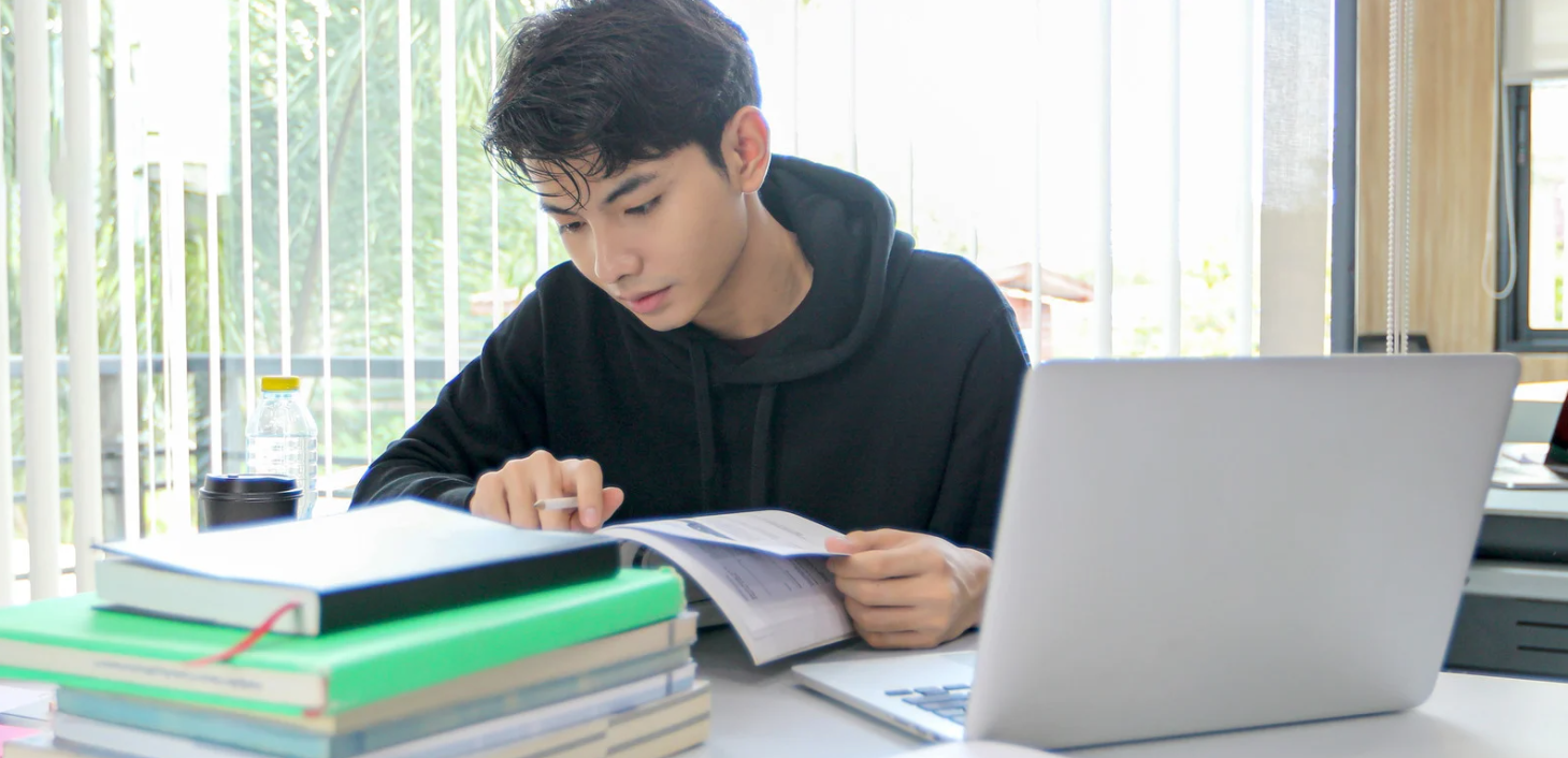 Young person with a laptop and an array of study materials.