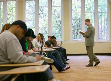 Teacher in suit standing in front of seated row of students.