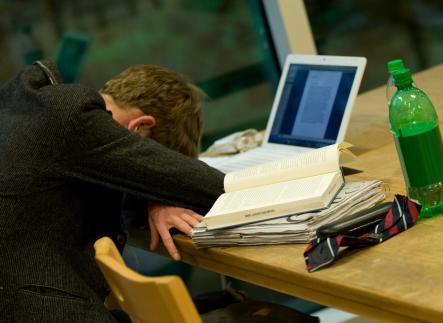 Photo of a student with his head on the desk on front of his laptop resting from study exhaustion