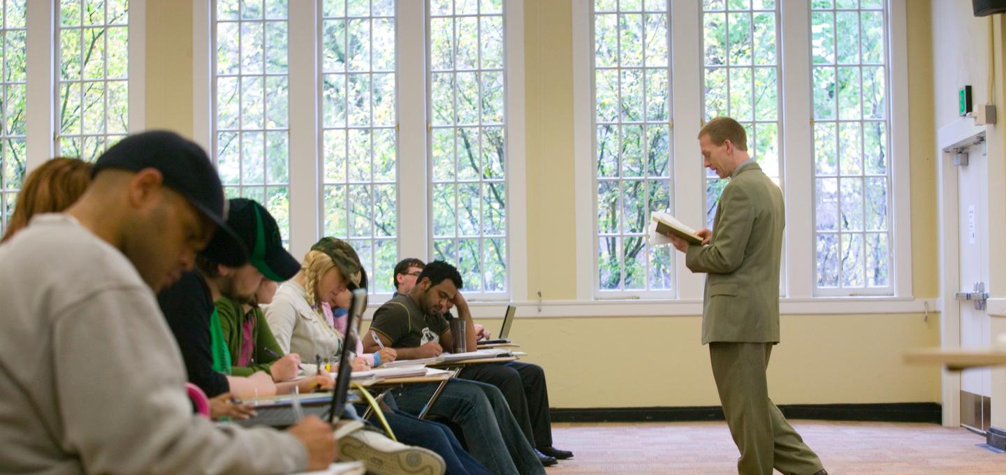 Teacher in suit standing in front of seated row of students.