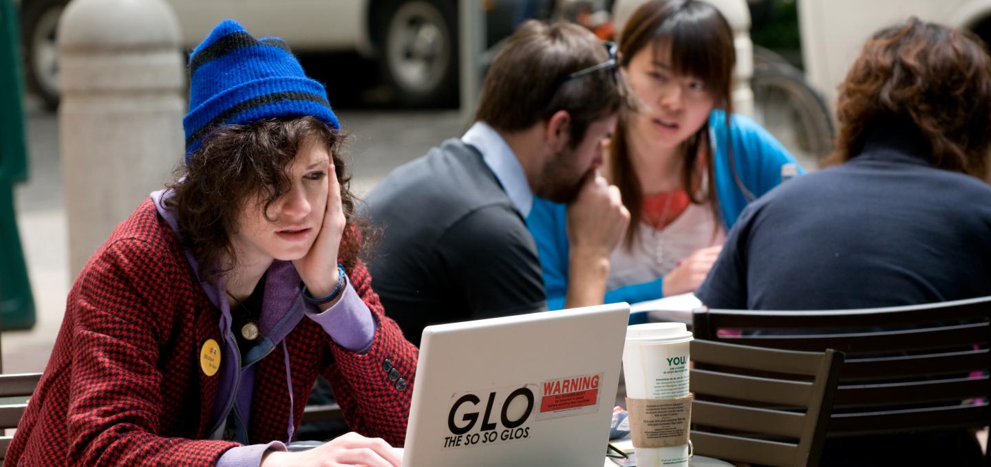 Student sitting in front of a laptop at a small table with face resting on one hand