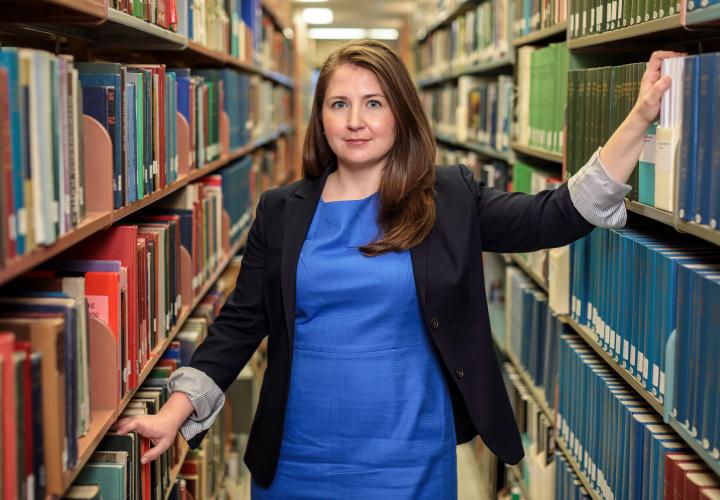 Female-identified faculty member of the Sociology department standing amongst the library bookshelves