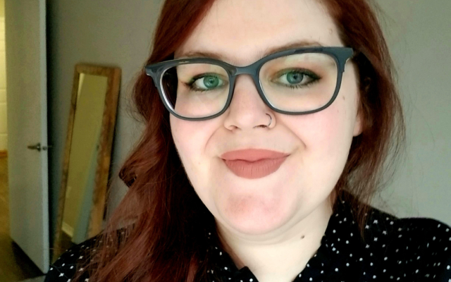 Female-identified person with long, red hair and glasses, wearing a black shirt.