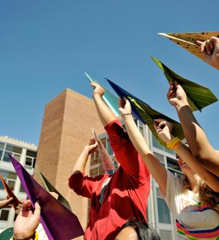 Group of students holding multicolored paper airplanes in the air.