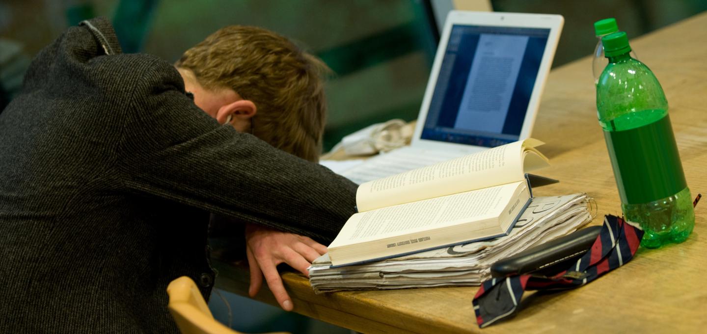 Photo of a student with his head on the desk on front of his laptop resting from study exhaustion