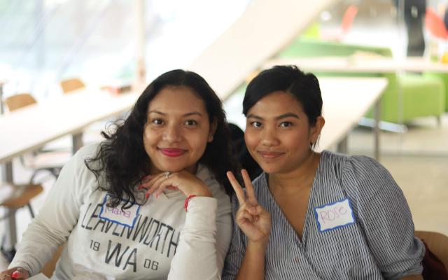 Student leaders smile for the camera while one holds up the peace sign. They are looking through magazines for a collage project.