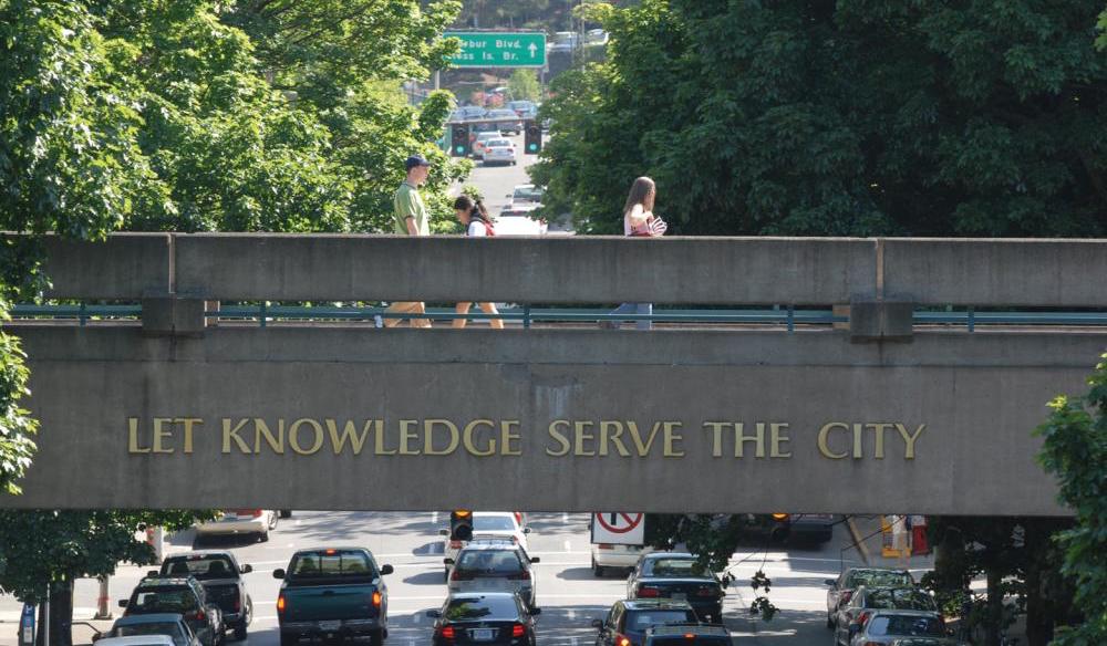 Image of students walking across PSU skybridge above SW Broadway with the words "Let Knowledge Serve the City" on the bridge