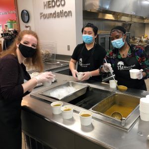 Three students wear masks while serving up food at Blanchet House