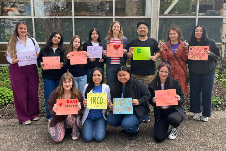Student Leaders for Service members stand facing the camera holding up signs that list the name of the community partner they are serving with