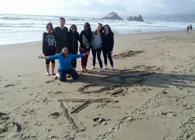 Seven students on an Alternative Spring Break trip pose for a picture on the beach in front of the letters "ASB" in the sand
