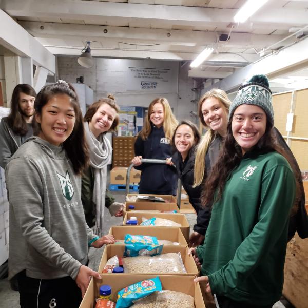 Smiling students stand around boxes of food they have packed for Sunshine Division food pantry