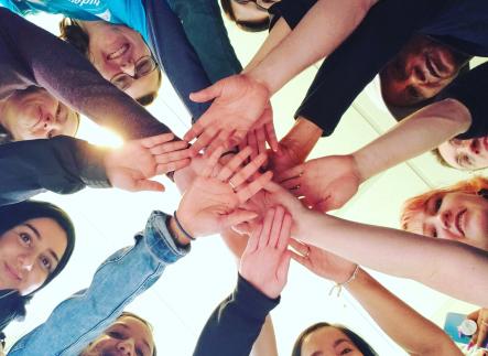 Many students in a circle with their hands outstretched and stacked on top of each other