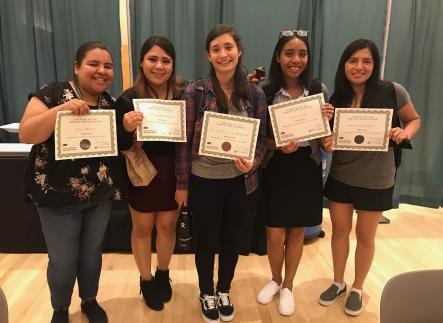 Five students stand facing the camera holding up certificates of service recognition