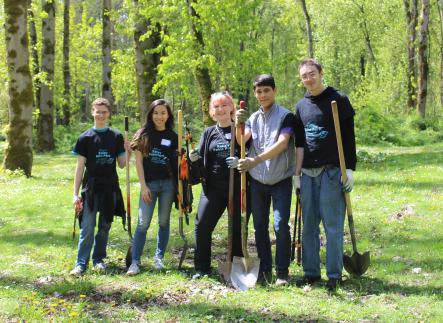 Five students stand in a park holding shovels at a service project