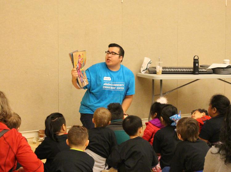 A volunteer wearing a blue shirt reads a book allowed to a group of young children