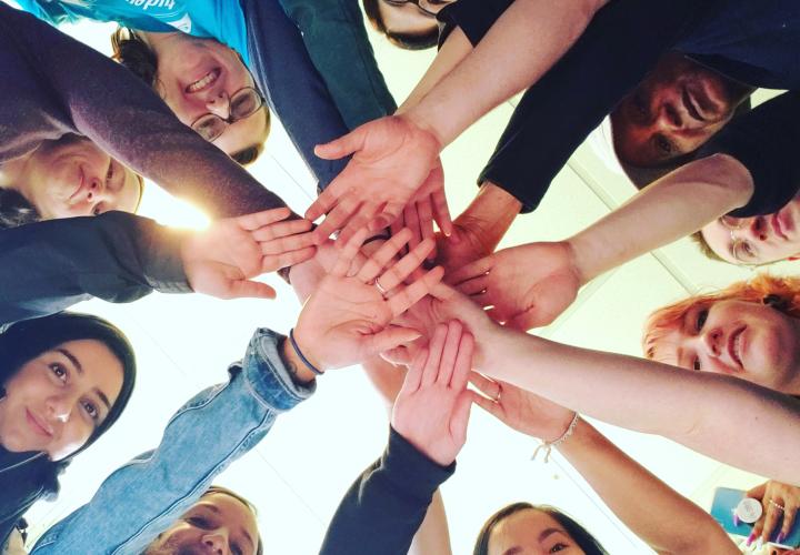 Many students in a circle with their hands outstretched and stacked on top of each other