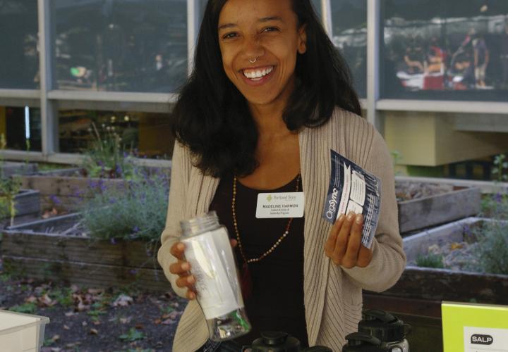 Student smiles as they hold up a flyer and a water bottle behind a tabling table at Party in the Park
