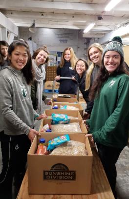 Smiling students stand around boxes of food they have packed for Sunshine Division food pantry